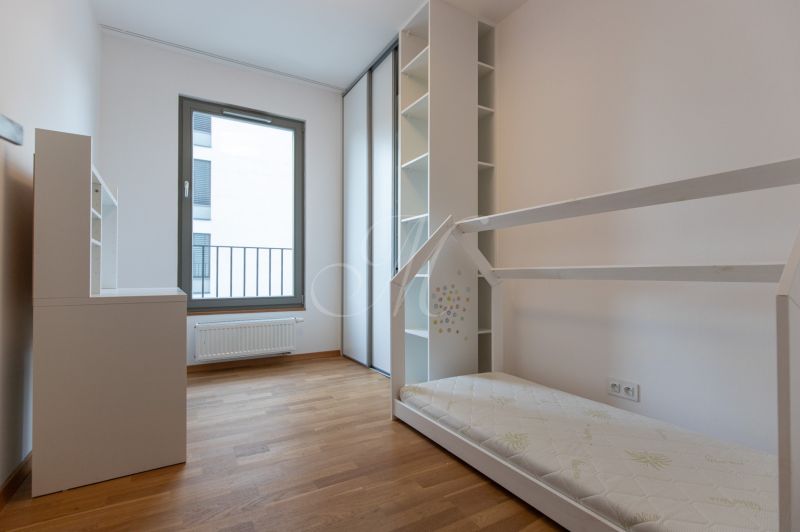 Children's room in a 3-room apartment with a bed and white furniture on a wooden decor floor.