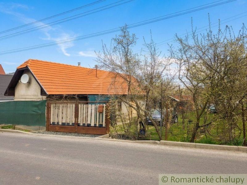 A family house in Stožok with a red roof, a fence, and a garden near the road.