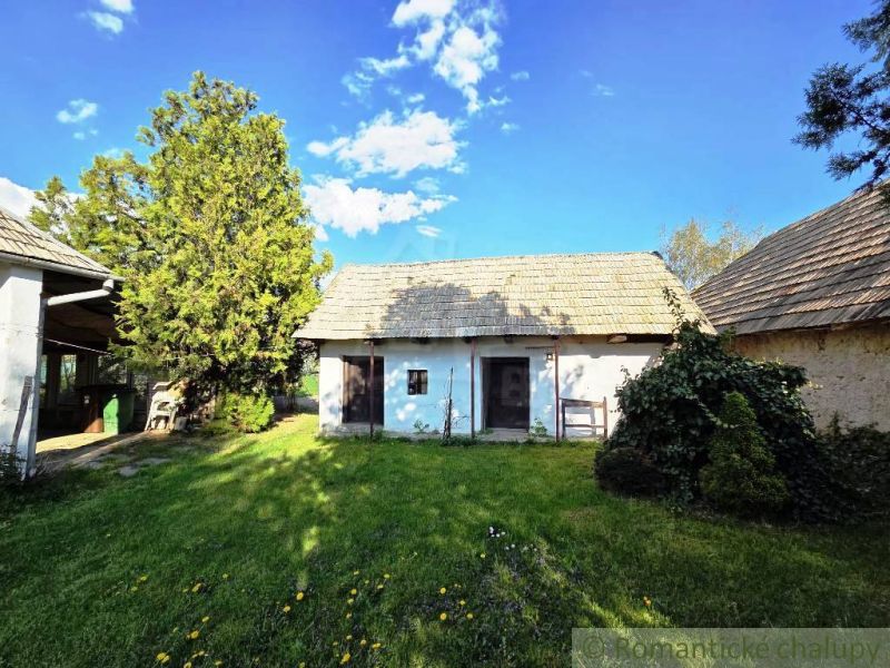 A cottage in Šahy with a shingle roof, a large garden, and trees.