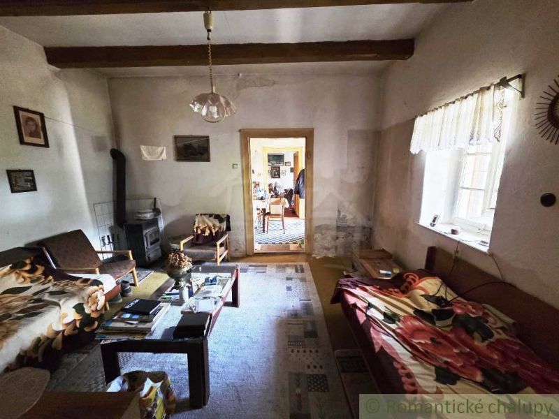 Living room in a cottage with a sofa, carpet, table, and wooden beams on the ceiling.