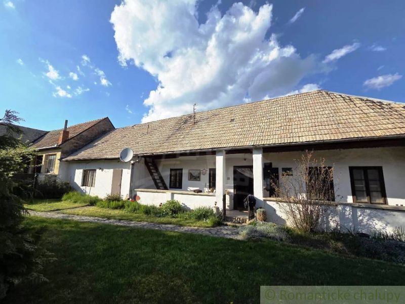 A cottage in Šahy with a large roof and a white facade in the countryside.