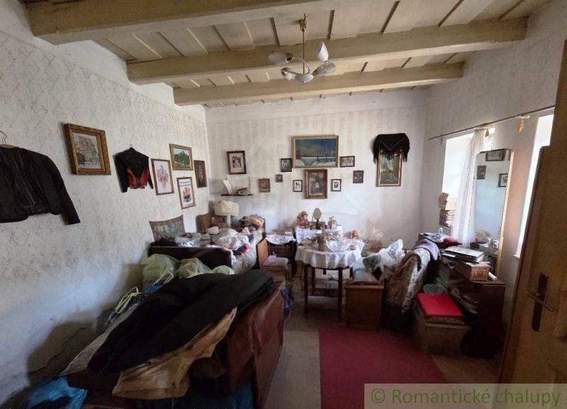 Room in a cottage with many antiques, paintings, and a wooden beam ceiling.