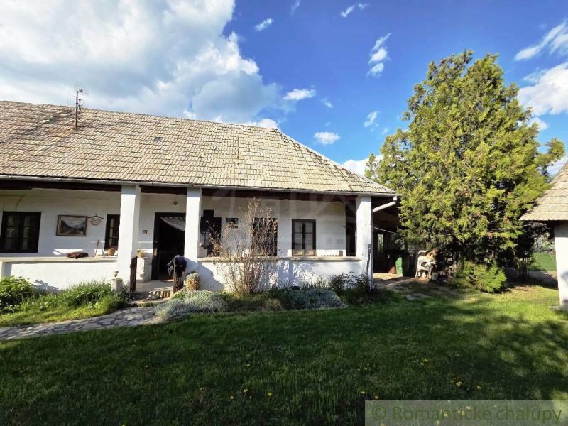 A cottage in Šahy with white walls and a traditional roof surrounded by greenery.
