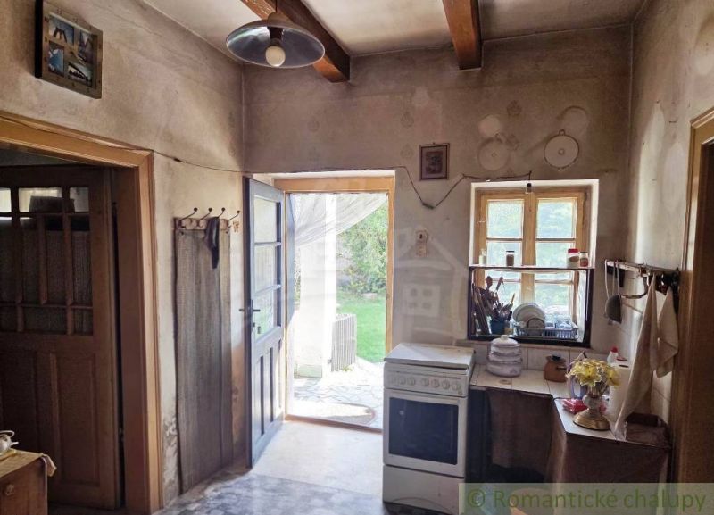 Rustic kitchen in a cottage with wooden beams, a stove, and a view of the garden.