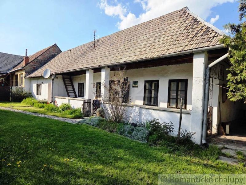 A traditional cottage in the town of Šahy with a white facade and a garden full of greenery.