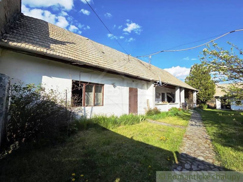 A cottage in Šahy with a white facade, a sloping roof, and a paved walkway.