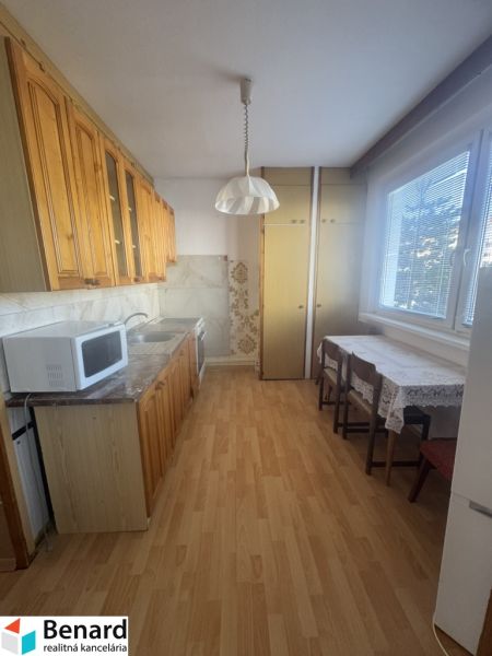 A kitchen unit with upper cabinets, a microwave, and a wooden decor floor in a 3-room apartment.