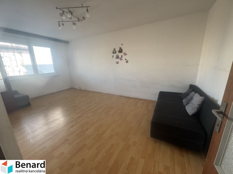 Living room with wood-patterned flooring, a sofa, and a large window in a three-room apartment.
