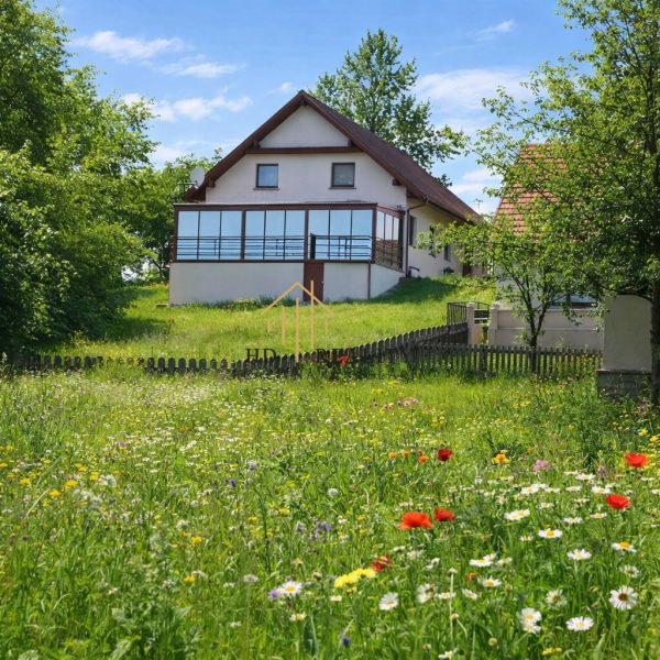A family house in Oravská Lesná bordered by a flowery meadow and a wooden fence.