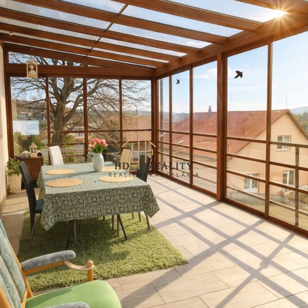 A glass-enclosed veranda in a family house with a dining table and a view.