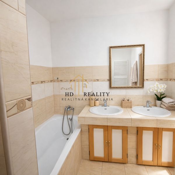 A bathroom in a family house with a bathtub, two sinks, and a mirror above them.