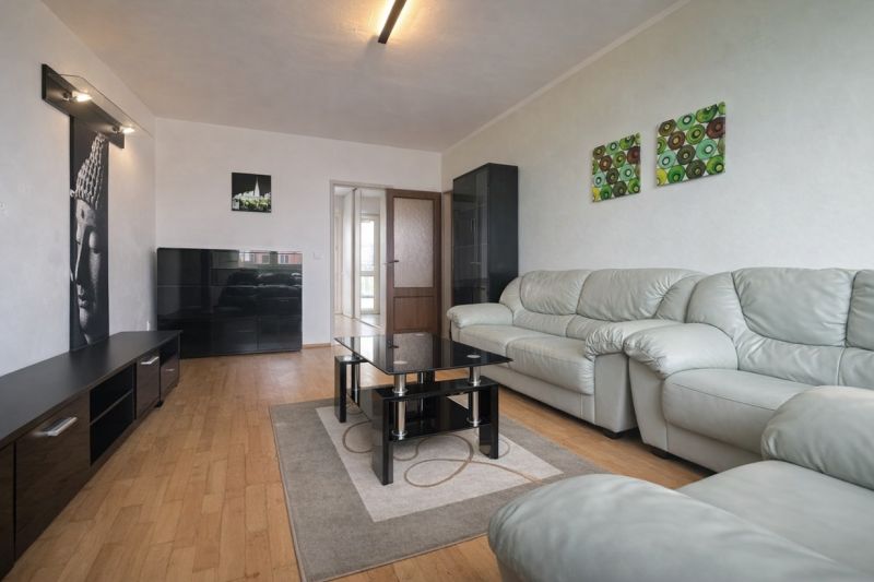 Living room with wood-patterned flooring, a sofa, and paintings, in a three-room apartment.