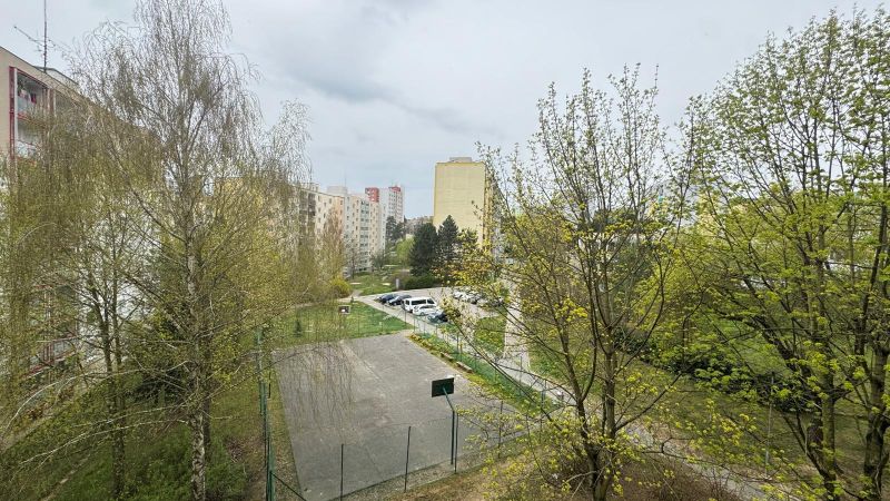 A view of the housing estate in Trenčín on Mateja Bela with a parking lot and a playground between the apartment buildings.