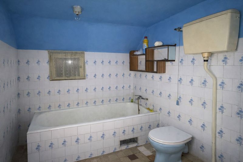 A bathroom in a family house with a blue bathtub, tiles, and a toilet.