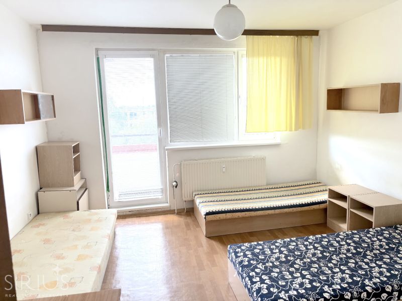 A studio apartment with a wooden floor, beds, and furniture.