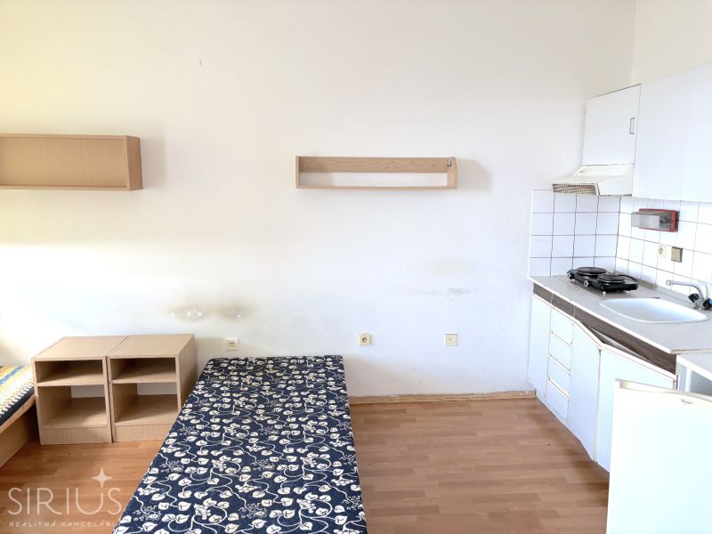 Studio apartment with a kitchenette, bed, and wooden decor flooring.