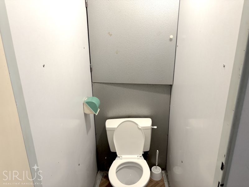 A bathroom in a studio apartment with white walls and a floor with a wood design.