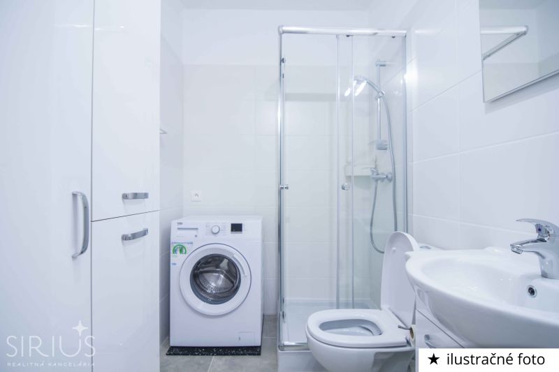 A bathroom in a studio apartment with a washing machine, shower, and sink in white tones.