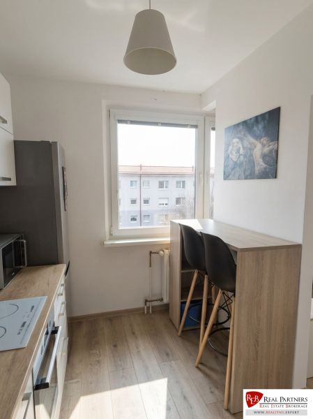 A kitchen in a studio apartment with a wood-patterned floor and bar seating.