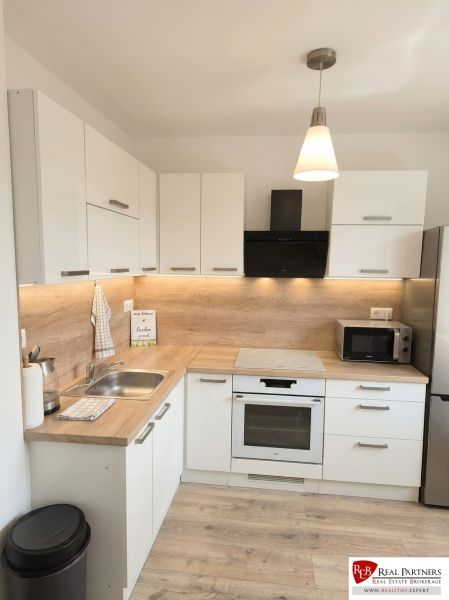 A kitchen in a studio apartment with light cabinets and a wood-patterned floor.