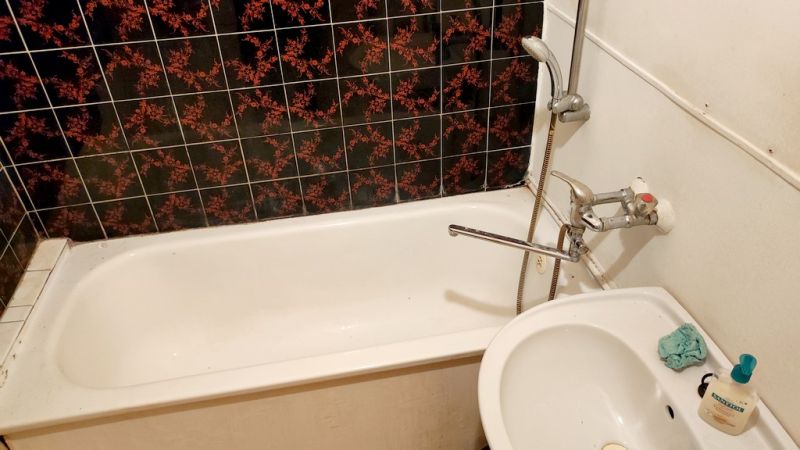A bathroom in a studio apartment with a bathtub and a sink, dark patterned tiles.