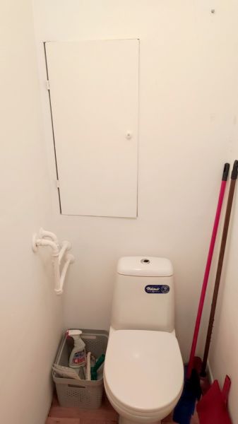 Toilet with storage space above the tank in a studio apartment, floor with wooden decor.