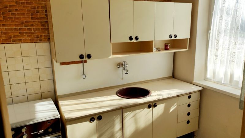 A kitchen in a studio apartment with tiles and light-colored furniture.