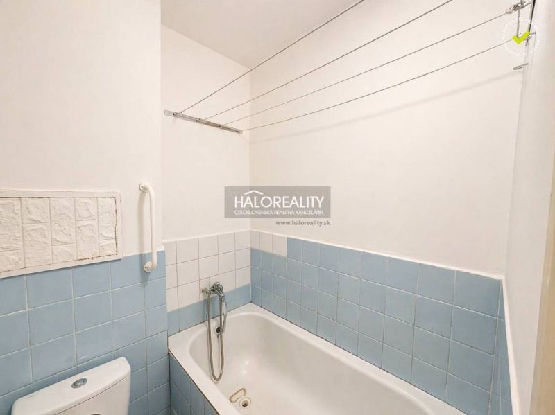 A bathroom with a bathtub and light blue tiles in a studio apartment.