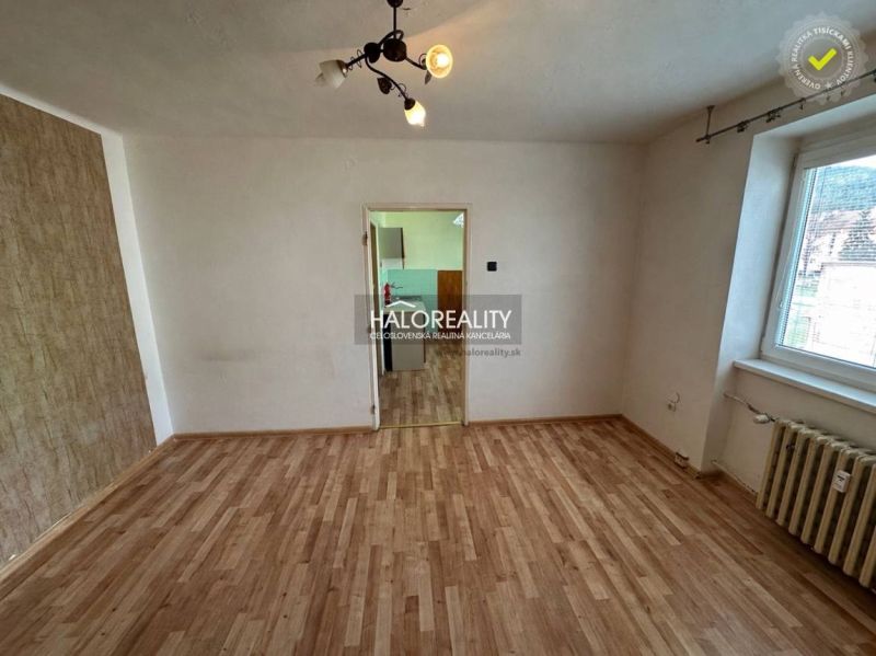 A room with a wooden floor design, a radiator, and a door to the kitchen in a studio apartment.