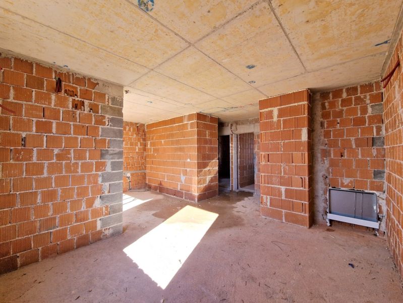 Unfinished interior of a 3-room apartment with brick walls and concrete floor.