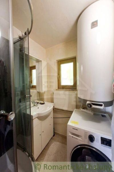 A bathroom with a washing machine, shower, and boiler in a family house.