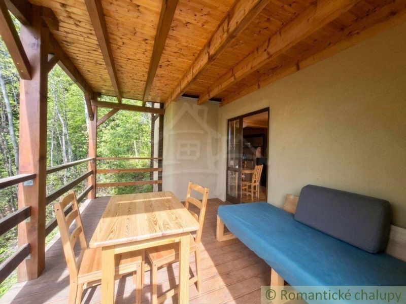 The veranda of a family house in Cinobana with seating and a wooden table by the forest.
