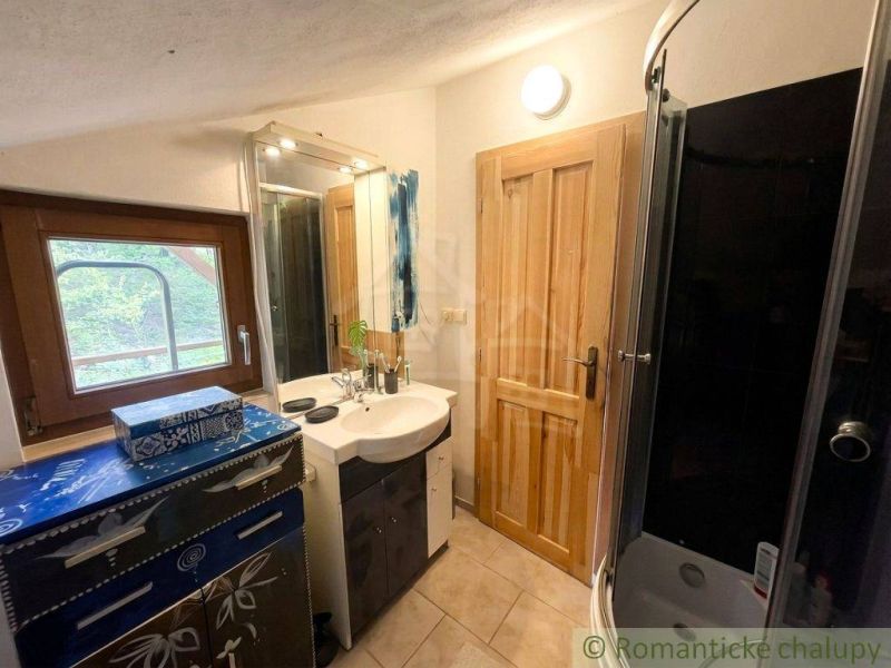 Bathroom with a sink, shower, and window, decorated cabinet, light walls.