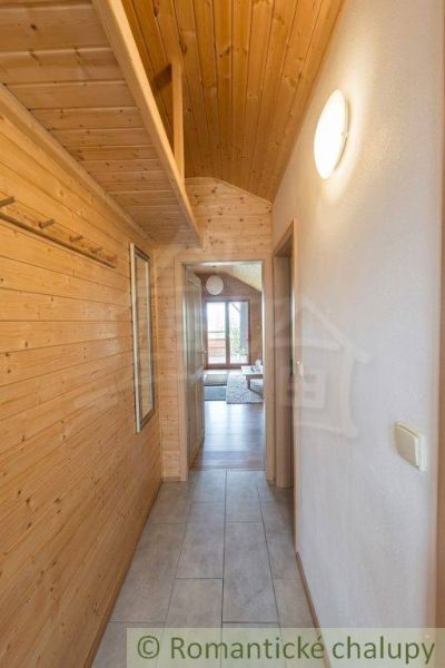 A narrow hallway with wooden paneling and a view into the living room of a family house.