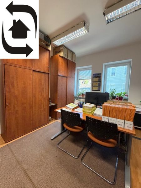 Offices with wooden furniture, documents on the table, two windows, and hanging ceiling lights.