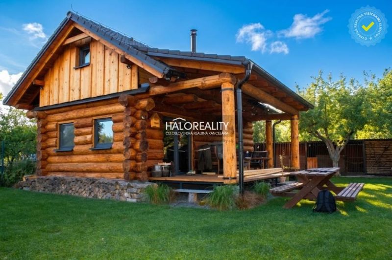 A wooden cottage in Piešťany with a terrace and garden seating, surrounded by greenery.