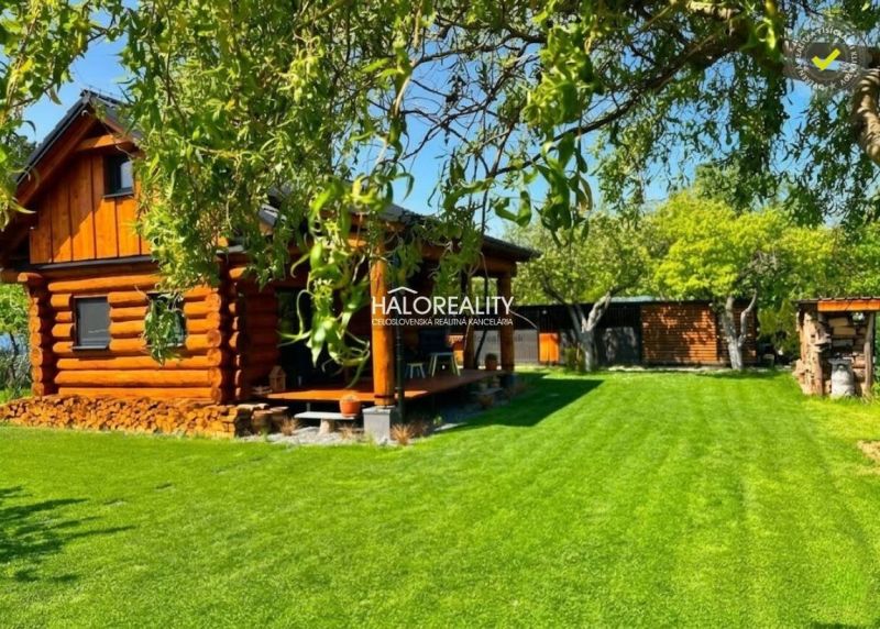 A wooden cottage in Piešťany with a landscaped garden and trees under the summer sky.