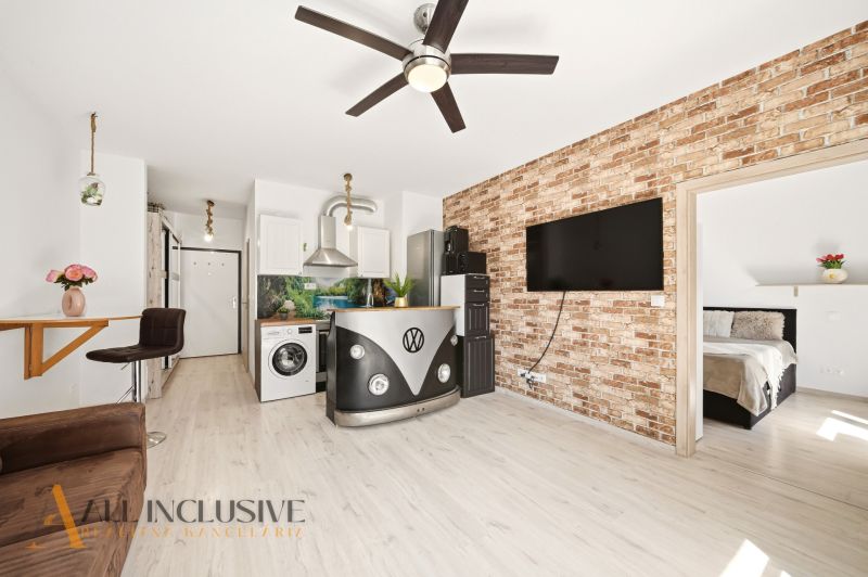 A two-room apartment with a wooden decor floor, brick walls, and a unique kitchen unit.