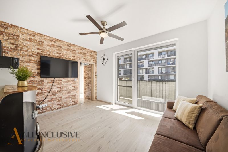 Living room with a brick wall, sofa, TV, and ceiling fan in a 2-room apartment.