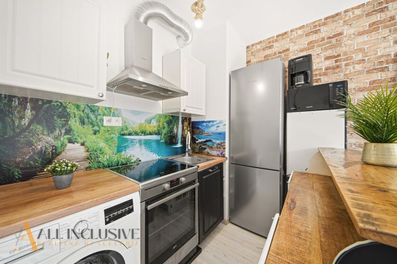 A kitchen in a 2-room apartment with a wooden decor floor and brick cladding on the wall.