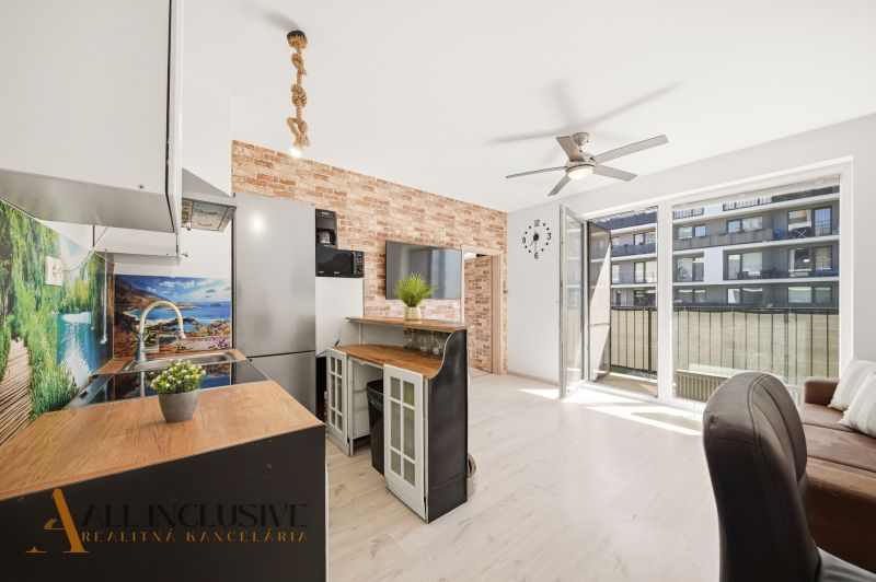 A kitchen in a 2-room apartment with a wooden decor floor and a brick wall.