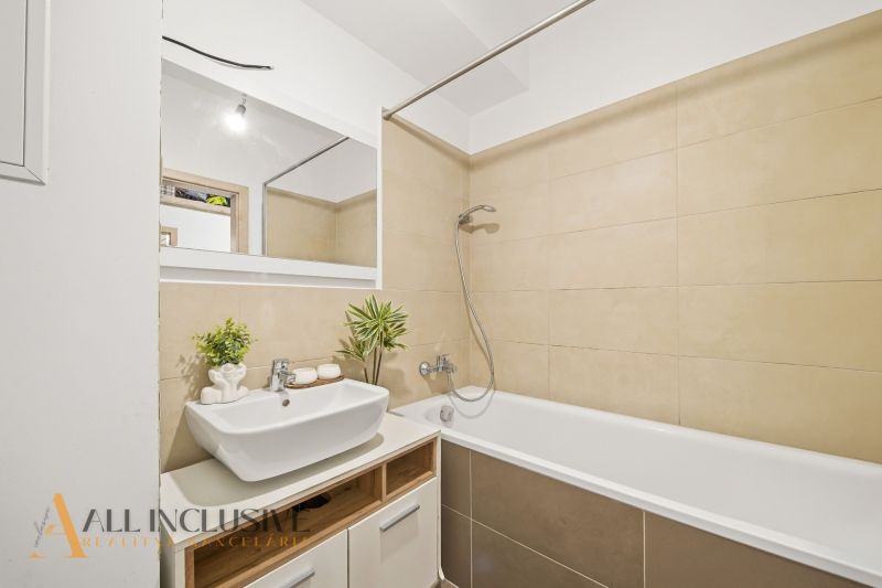 A bathroom with light tiles, a shower over the bathtub, and a sink in a 2-room apartment.