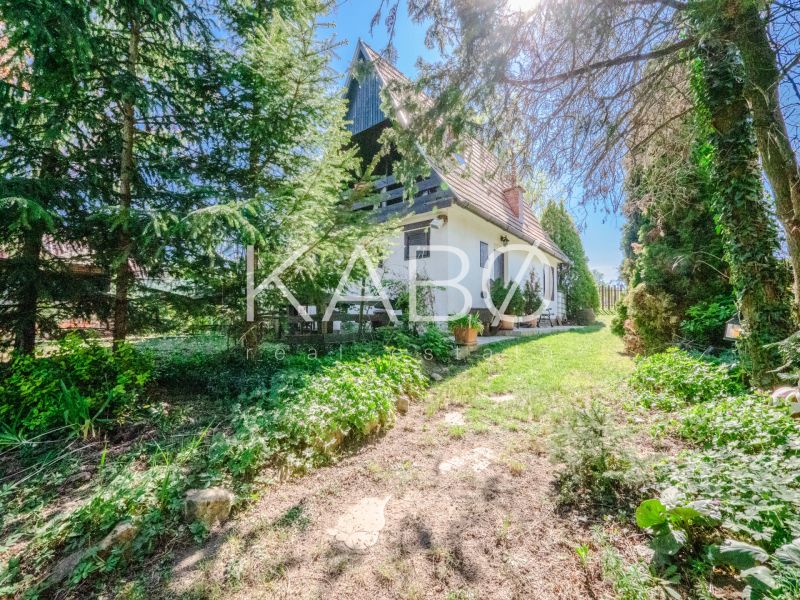 A cottage in Nitra surrounded by trees and a green lawn under a clear blue sky.