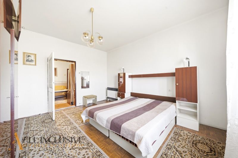 Bedroom in a family house with a double bed, striking carpets, and a wooden-patterned floor.