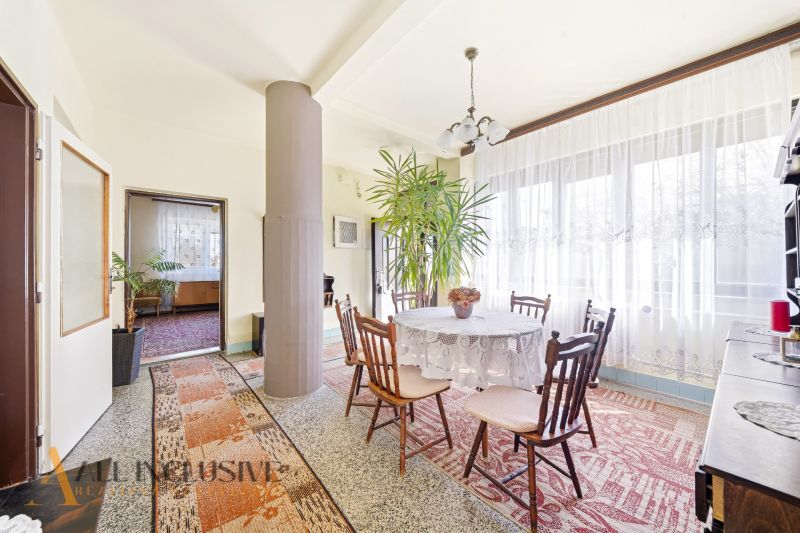 A dining room of a family house with a flower, a column, and a window with curtains.