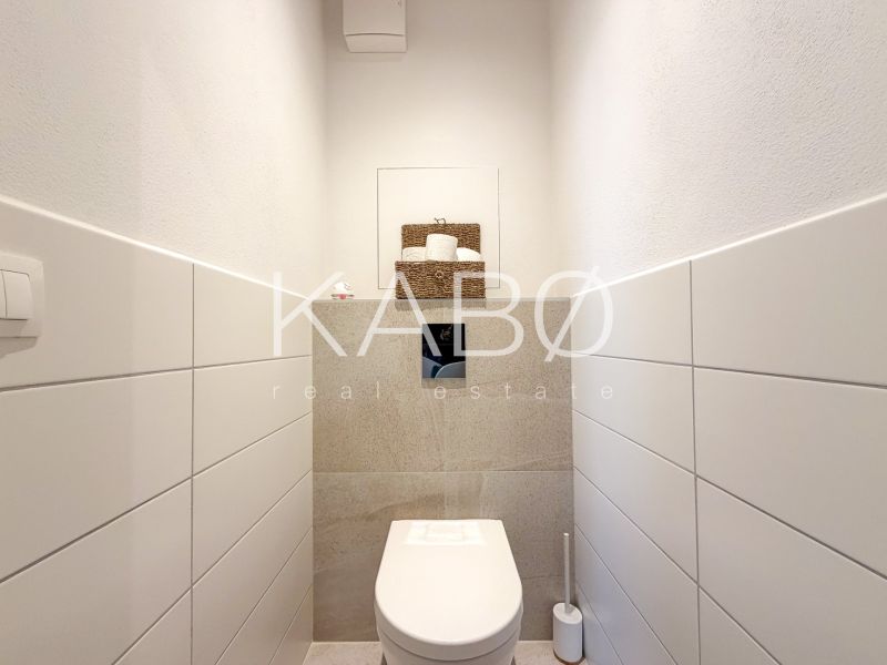 A toilet in a 2-room apartment with white tiles and storage space.