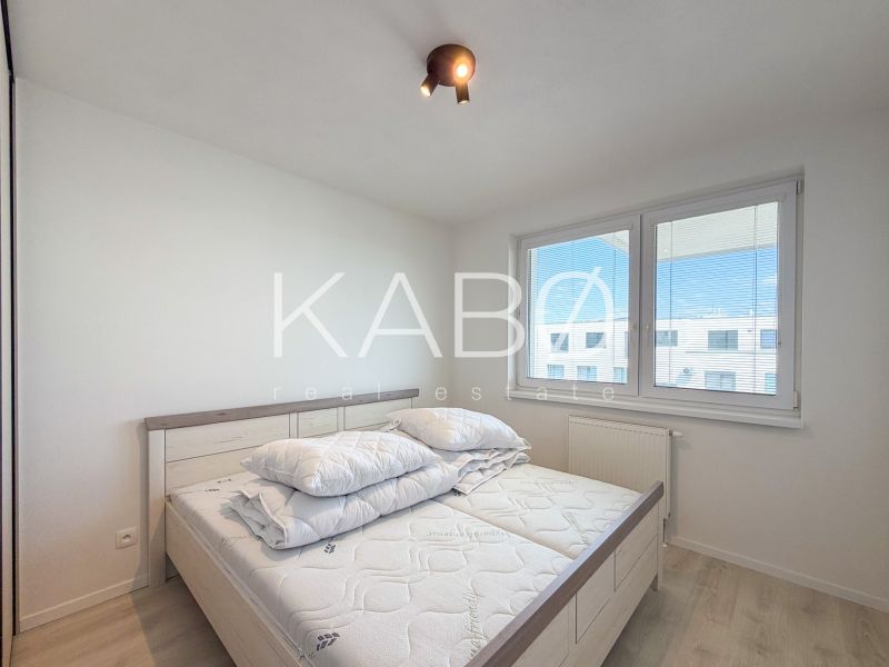 Bright bedroom in a two-room apartment with wood-patterned flooring and a window.