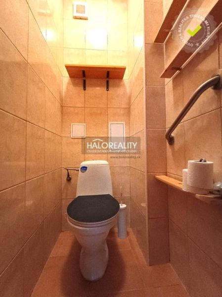A toilet with light tiles in a 2-room apartment, a handle on the wall, a shelf for toilet paper.