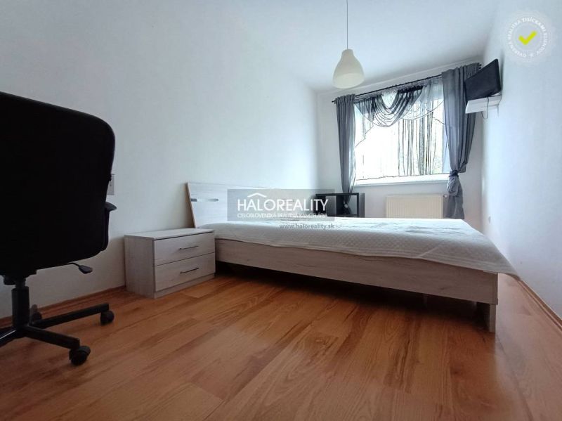 A bedroom in a two-room apartment with a wooden decor floor, a bed, and a chair.