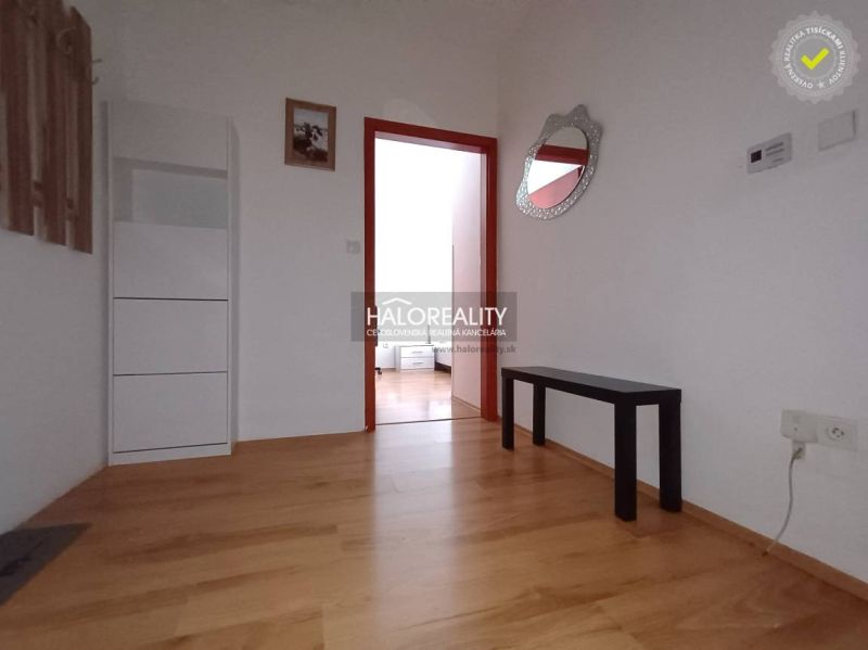 A hallway in a 2-room apartment with a wooden decor floor, simple furniture, and a mirror.